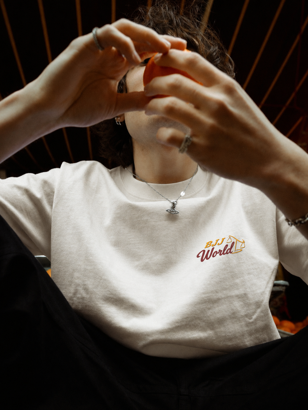 Cream tee from BJJ World with a small chest logo, worn against warm light.