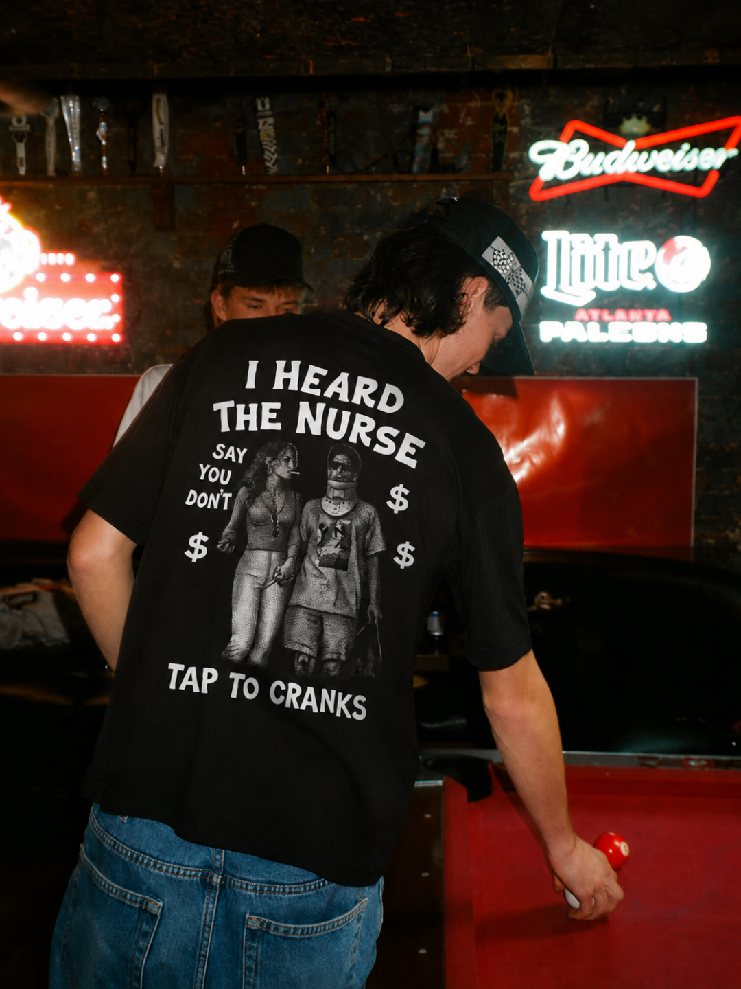 Black I Heard The Nurse tee from BJJ World, back print worn at a bar pool table.