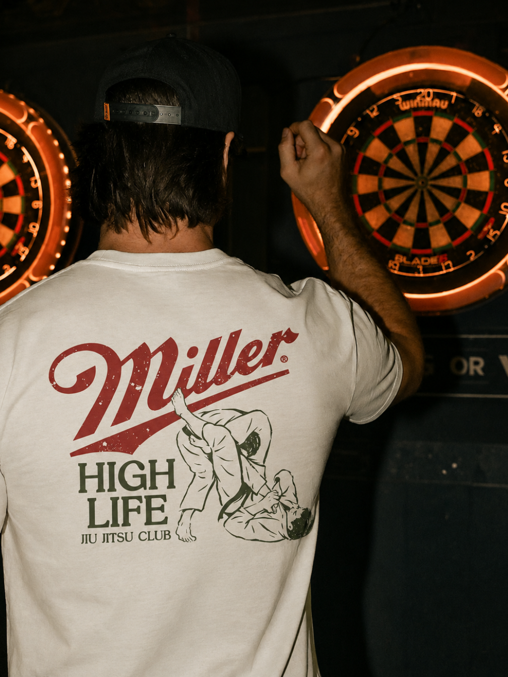 Cream Miller Jiu Jitsu Club tee from BJJ World, back print worn at a bar dartboard.